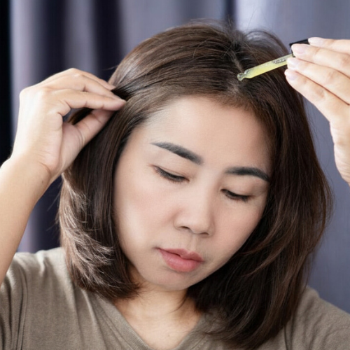 Woman adding drops of anidroba oil in her scalp against a neutral background